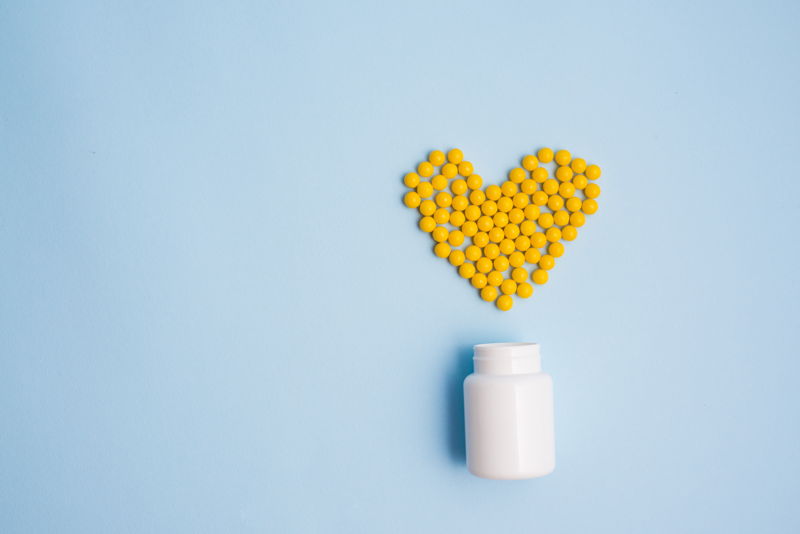 Corazón hecho por comprimidos amarillos al lado de un bote