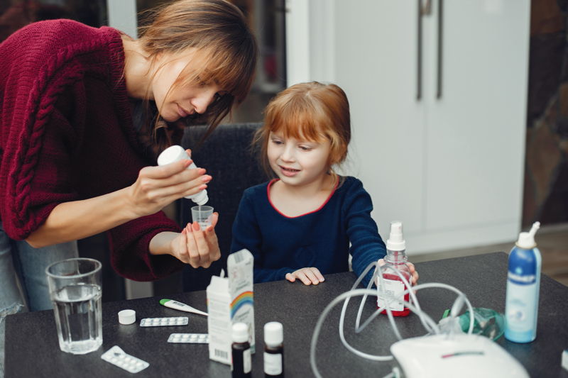 Mother giving medicine to her daughter at home