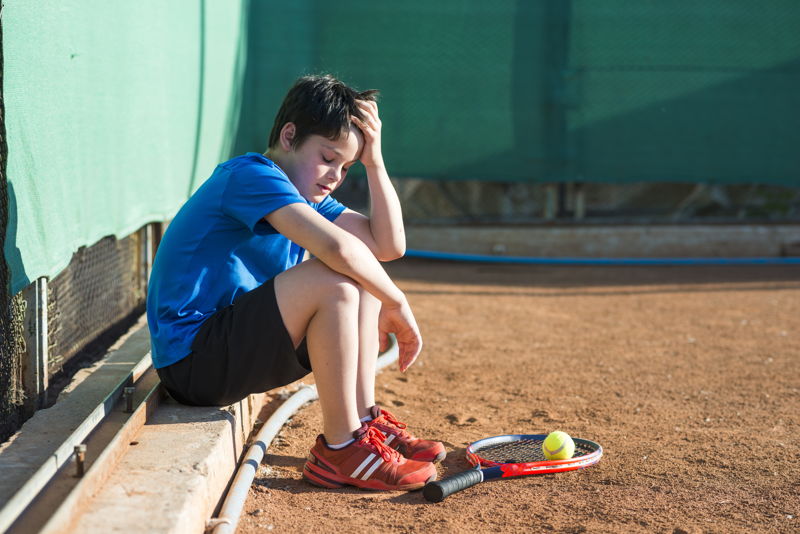 Niño triste y confundido sentado en el borde de un campo de tenis