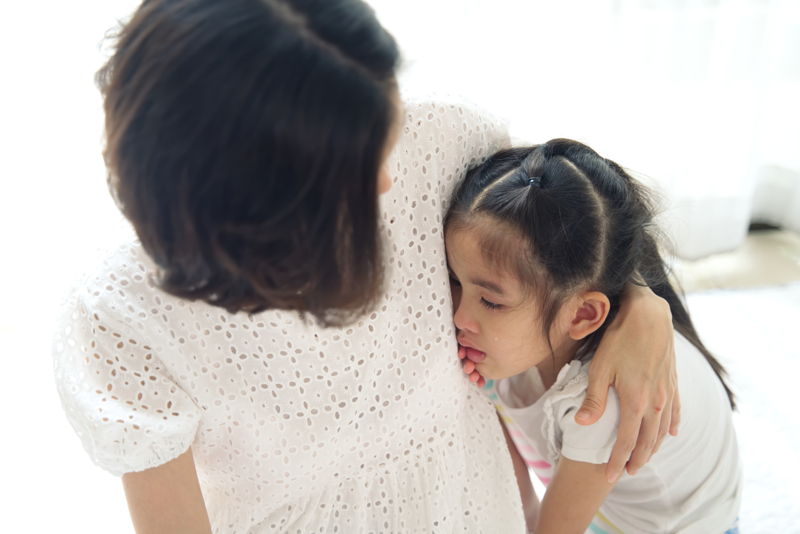 Niña apenada mostrando dolor y buscando consuelo en un abrazo con su madre