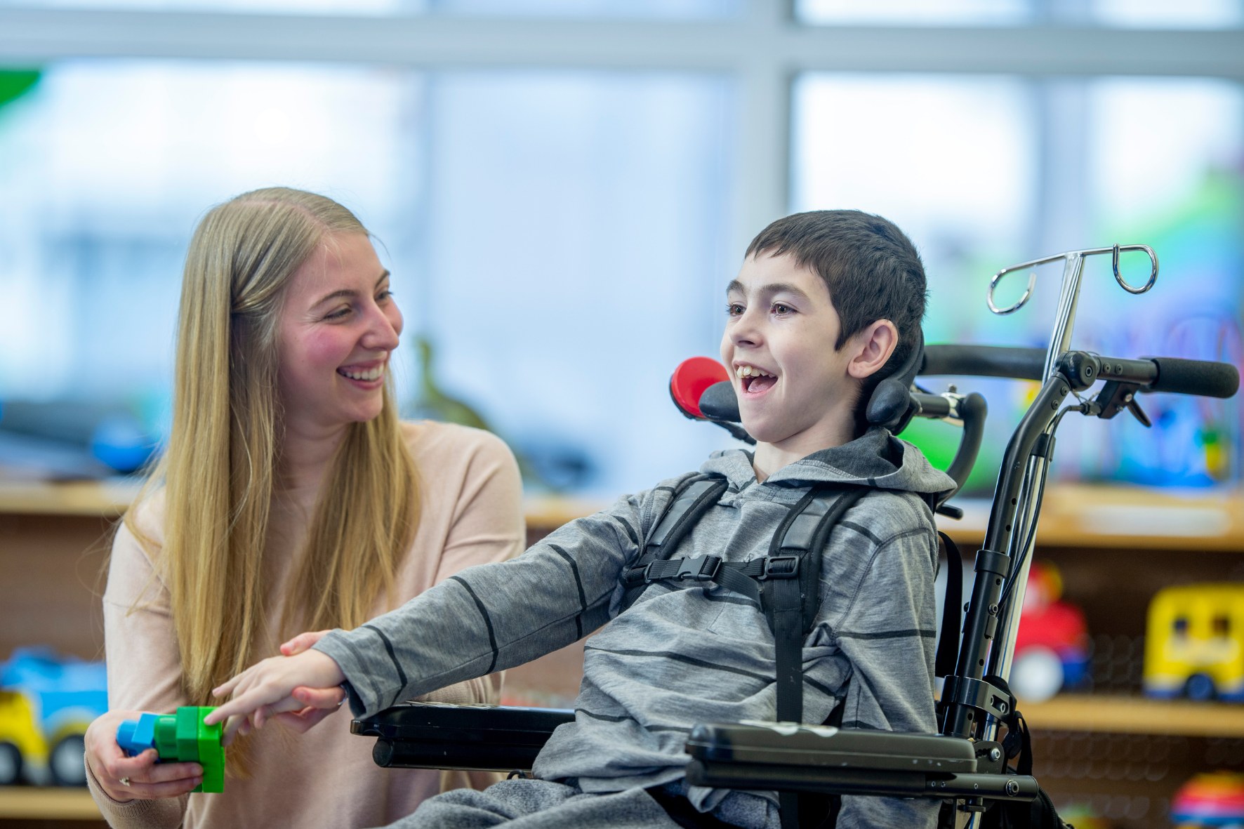 chica sonriendo jugando con niño sonriendo en silla de ruedas