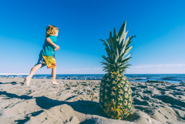Kid on the beach and a pineapple on the sand