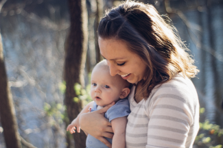 Mom laughing holding her small kid in the sunny woods