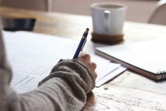 Person writing and with a cup of coffee on the desk