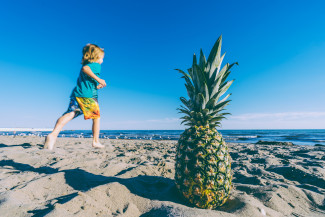 Summer holidays! Kid on the beach and a pineapple on the sand