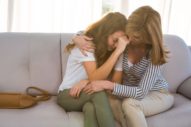 Madre abrazando a su hija que llora por la pérdida del hermano enfermo