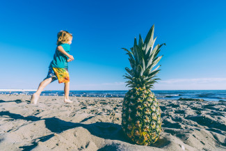 Kid on the beach and a pineapple on the sand