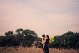 Mum and son kissing each other on a field and holding balloons